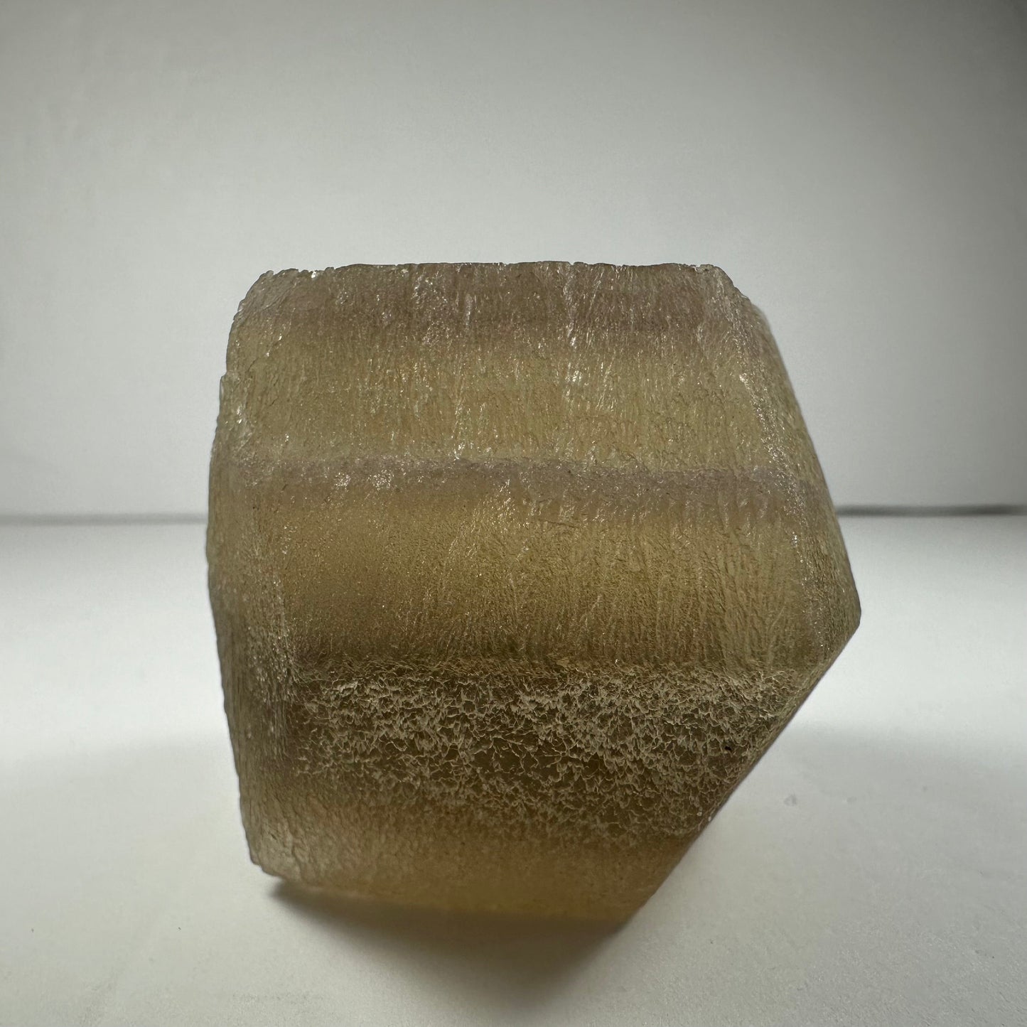 Polished fluorite dodecahedron with twelve pentagonal faces in banded green and purple, held in daylight — view 8