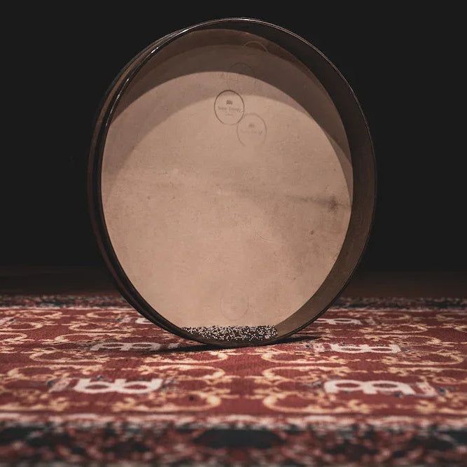 Ocean drum tilted on a patterned red rug with the plain natural-skin head facing the camera
