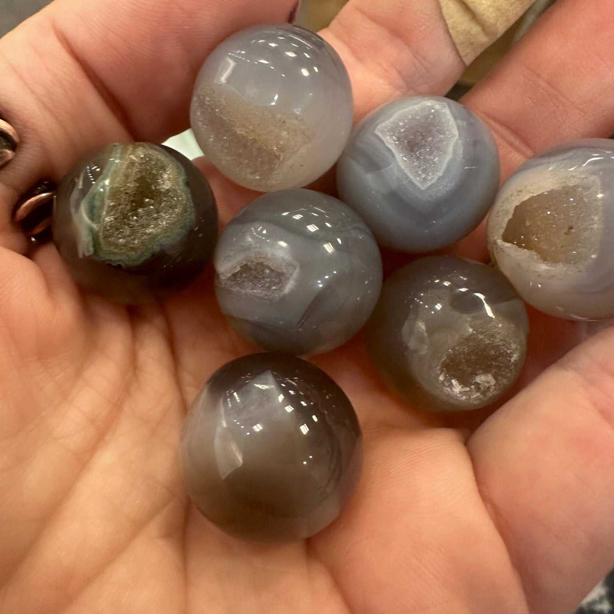 Small polished agate geode pocket sphere showing banded layers and a sparkling druzy cavity