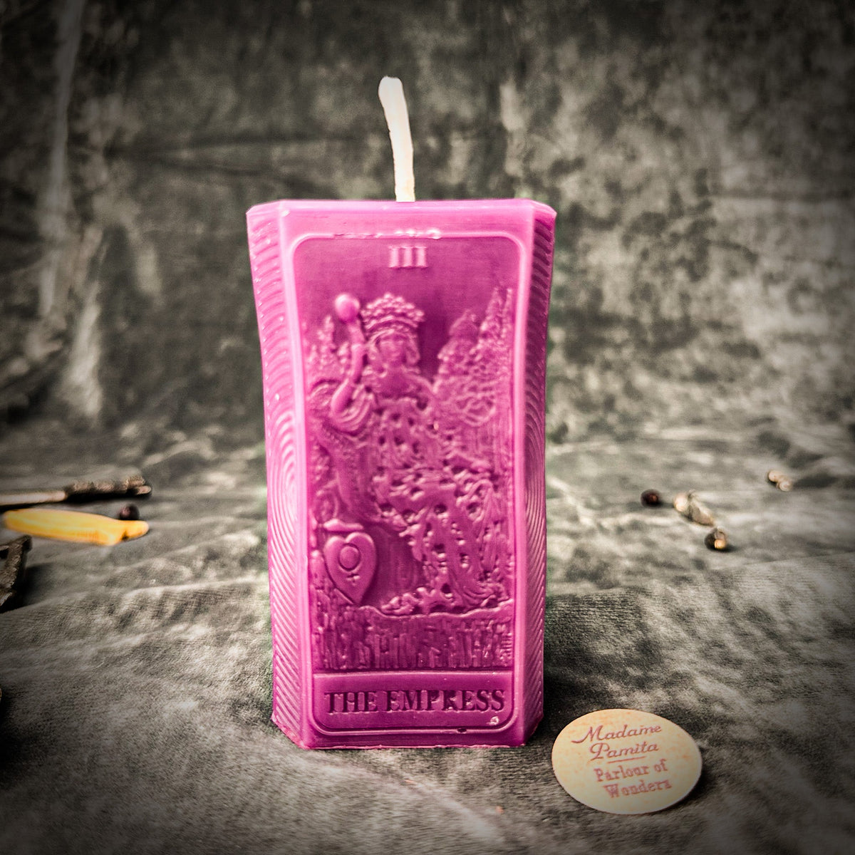 Vivid purple-pink beeswax The Empress tarot card candle on gray draped cloth