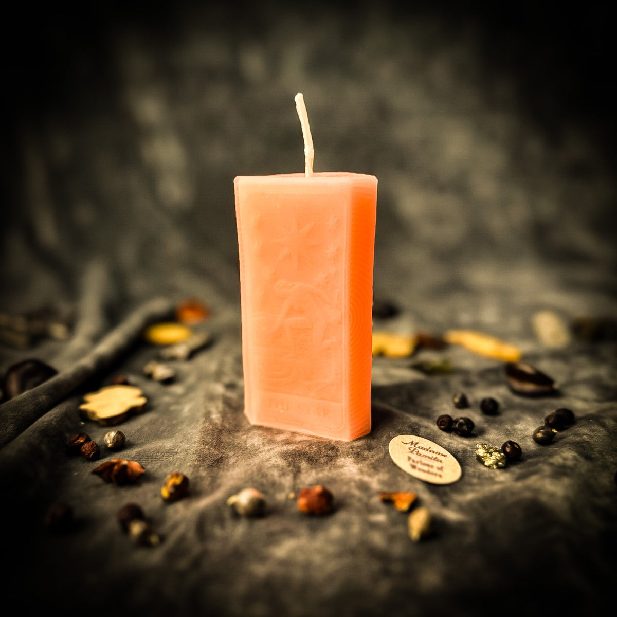 Pale peach beeswax The Star tarot card candle standing upright on gray fabric