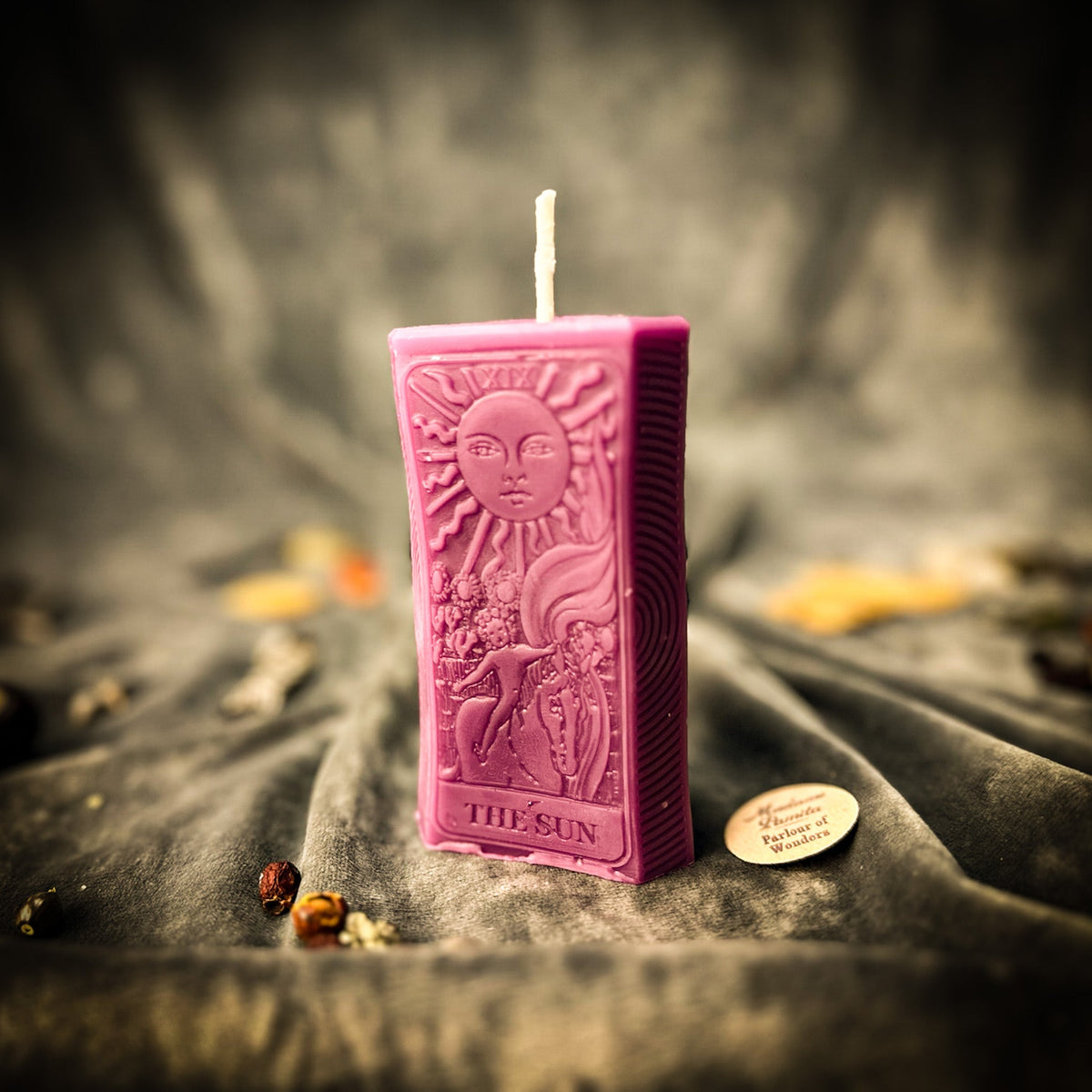 The Sun beeswax tarot candle in pink on draped gray fabric