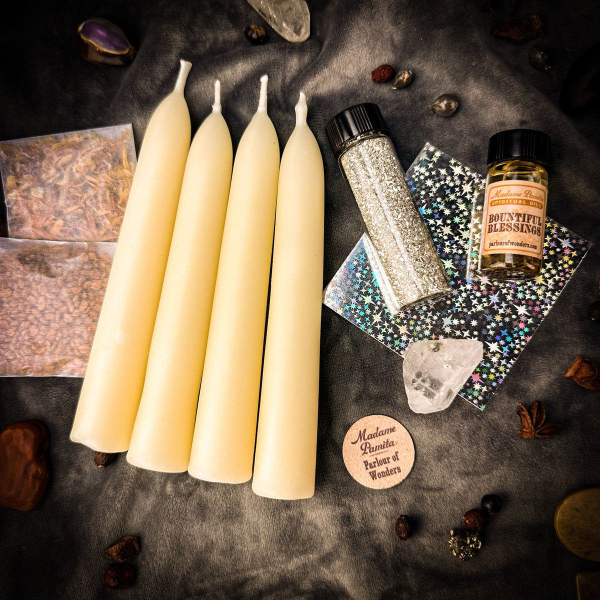 Miracles Candle Spell Booster Pack seen from above on dark stone: four cream beeswax tapers beside silver glass glitter, consecrated oil, sealed herb packets, holographic petition papers and a wooden Parlour of Wonders token.