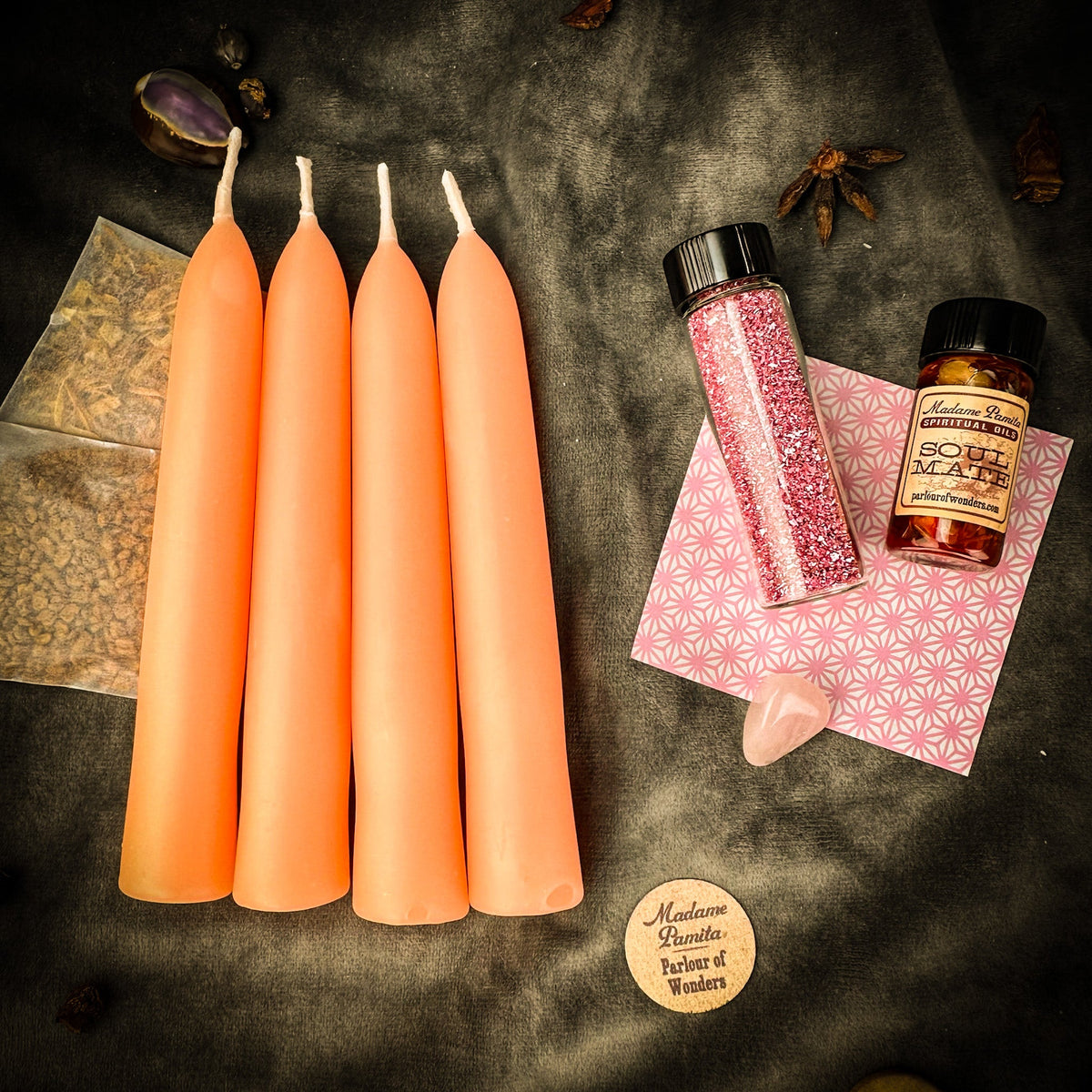 The same Romance booster pack on dark gray cloth under warm tungsten light, which reads the tapers a deeper coral; star anise and dried pods lie around the edges.