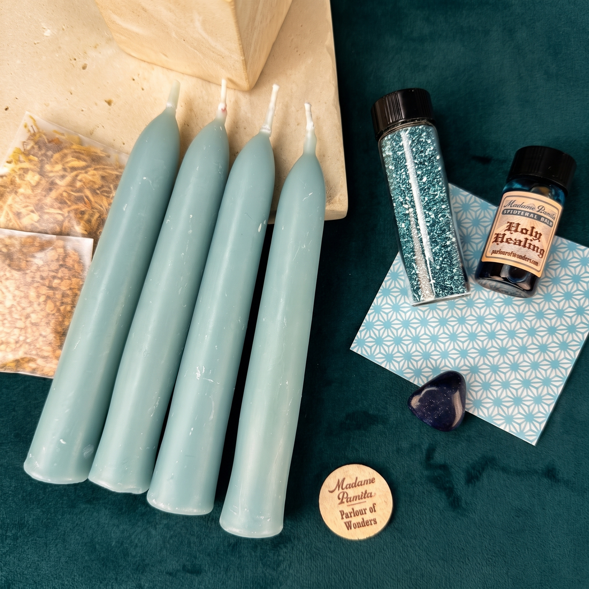 Healing Candle Spell Booster Pack: four pale blue beeswax taper candles with a bottle of Holy Healing oil, a vial of blue glass glitter, sealed herb packets, a tumbled stone and a patterned petition paper.