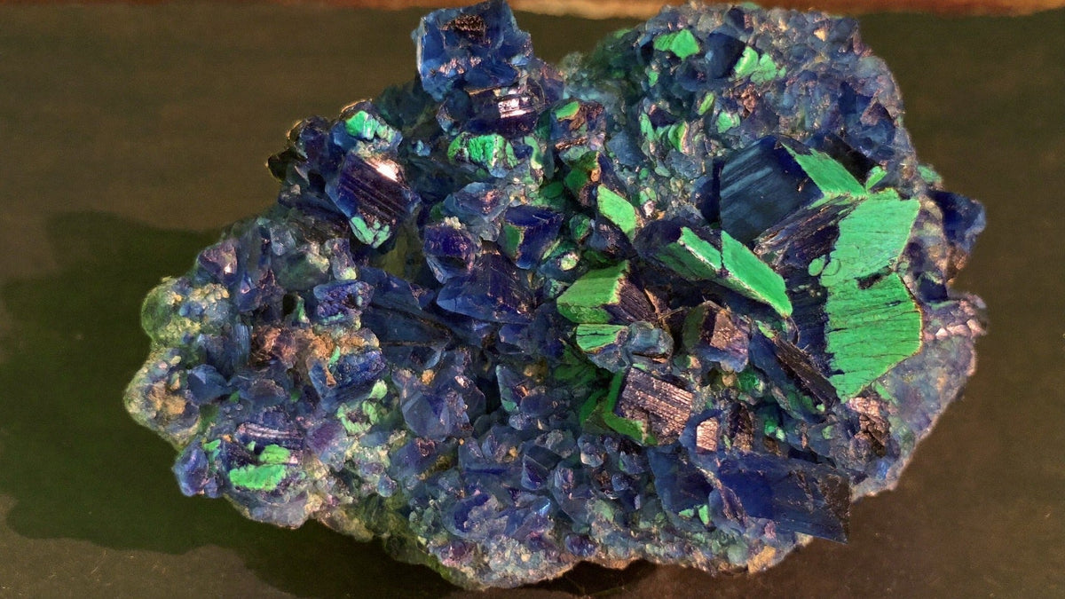 Close-up of an azurite specimen with deep blue glassy crystals and green malachite patches on dark slate