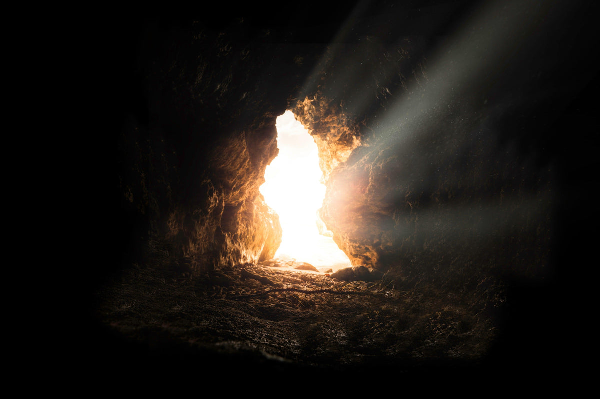 Sunlight streaming through a cave mouth into a dark underground chamber, the classic image of the inner descent