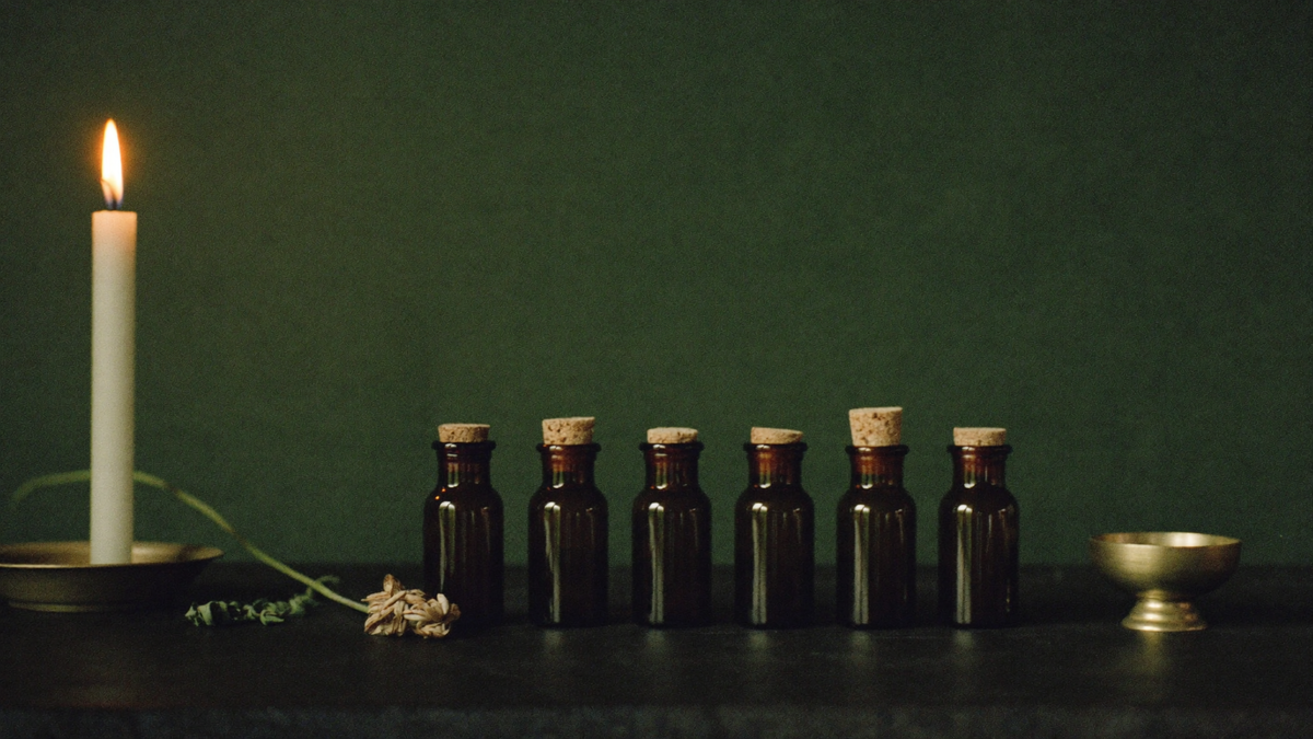 Row of amber glass bottles with cork stoppers beside a lit candle and a brass bowl on a dark surface
