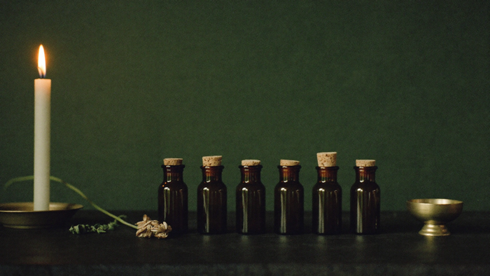 Row of amber glass bottles with cork stoppers beside a lit candle and a brass bowl on a dark surface