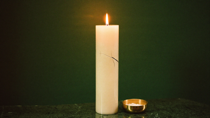 A tall vigil candle with a hairline crack in its side, burning on a dark green stone altar surface