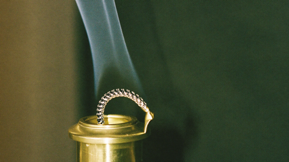 Smoke rising from a brass censer in warm candlelight against a dark green background