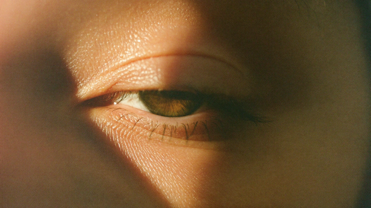 Close-up of a human eye with the upper eyelid half lowered, lit by warm candlelight from the left side