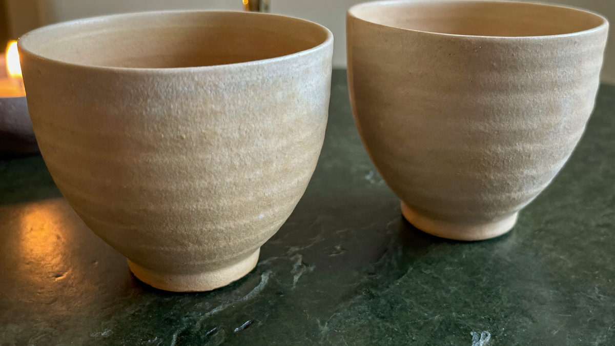 Two plain ceramic cups side by side on a dark green stone surface in warm candlelight