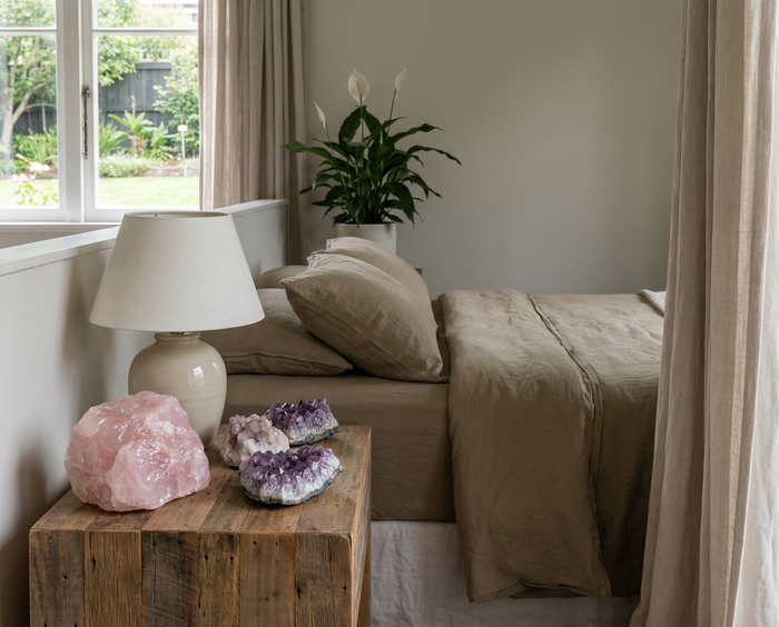 Bedroom nightstand with a rose quartz chunk and amethyst geodes beside a linen-dressed bed