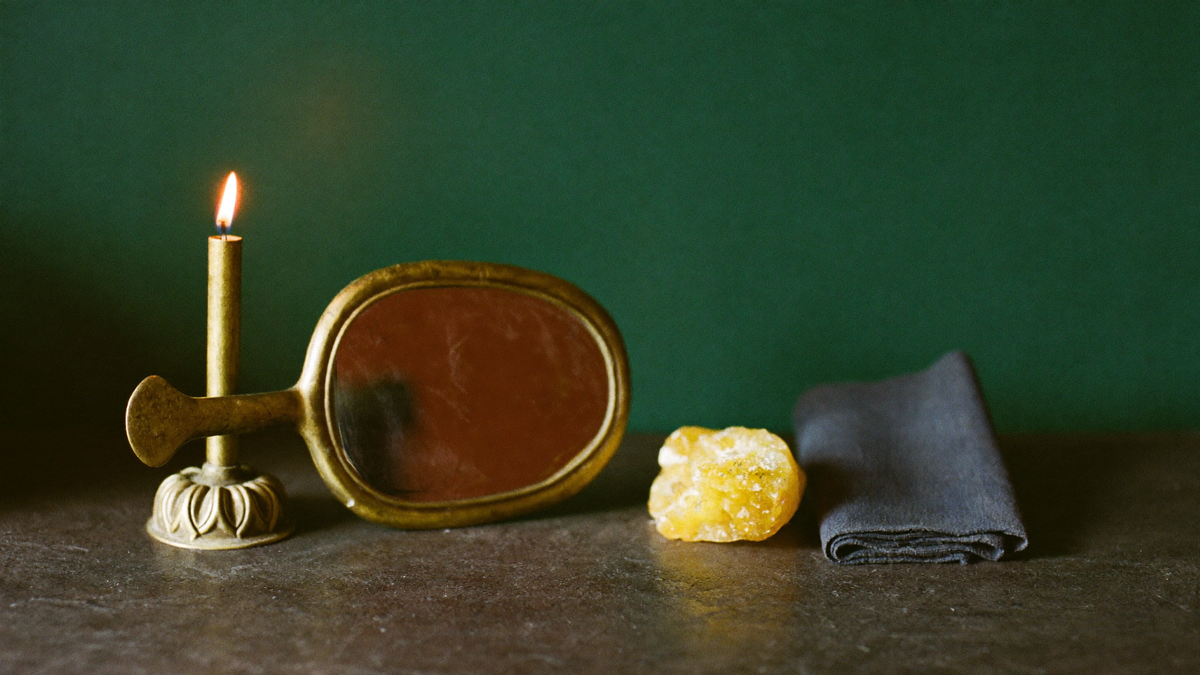 A brass candlestick, an antique hand mirror and a golden pyrite cluster on stone against a deep green wall