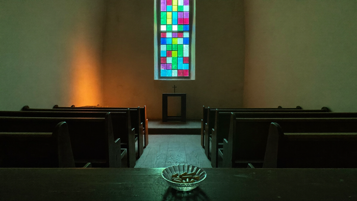Small chapel with wooden pews and a stained glass window, a glass bowl of capsules on the front pew