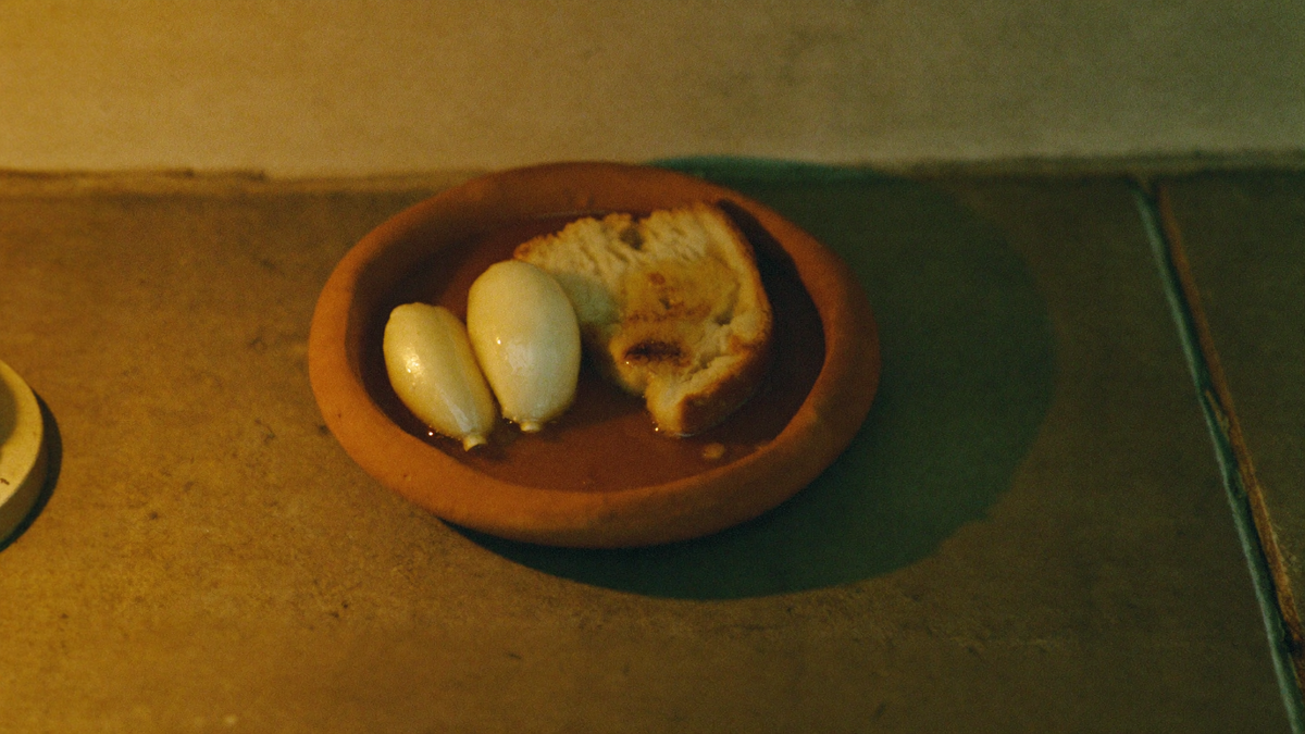 A small clay dish of garlic, bread and honey set down on a stone threshold in warm candlelight