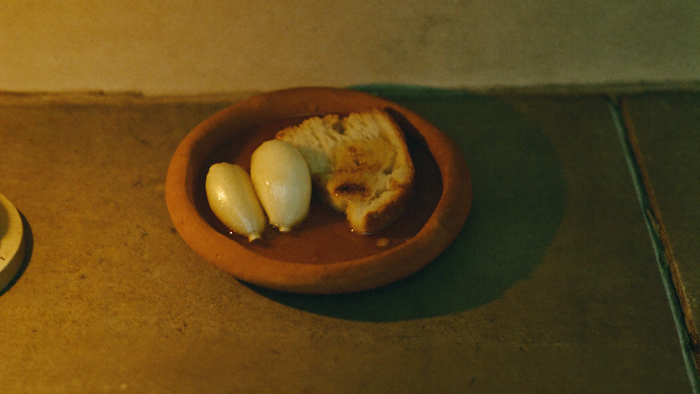 A small clay dish of garlic, bread and honey set down on a stone threshold in warm candlelight