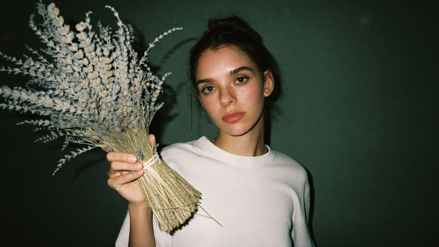 A young woman holding a tied bundle of dried herbs against a dark green wall