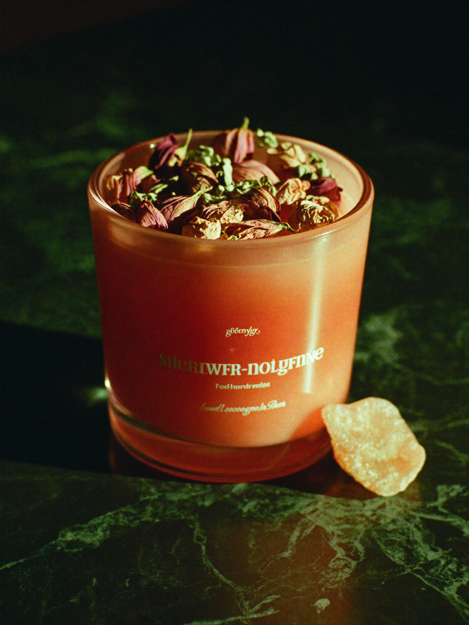 A Love Drawing ritual candle burning low on polished dark marble, its flame the brightest point against a deep emerald-green background falling into shadow.