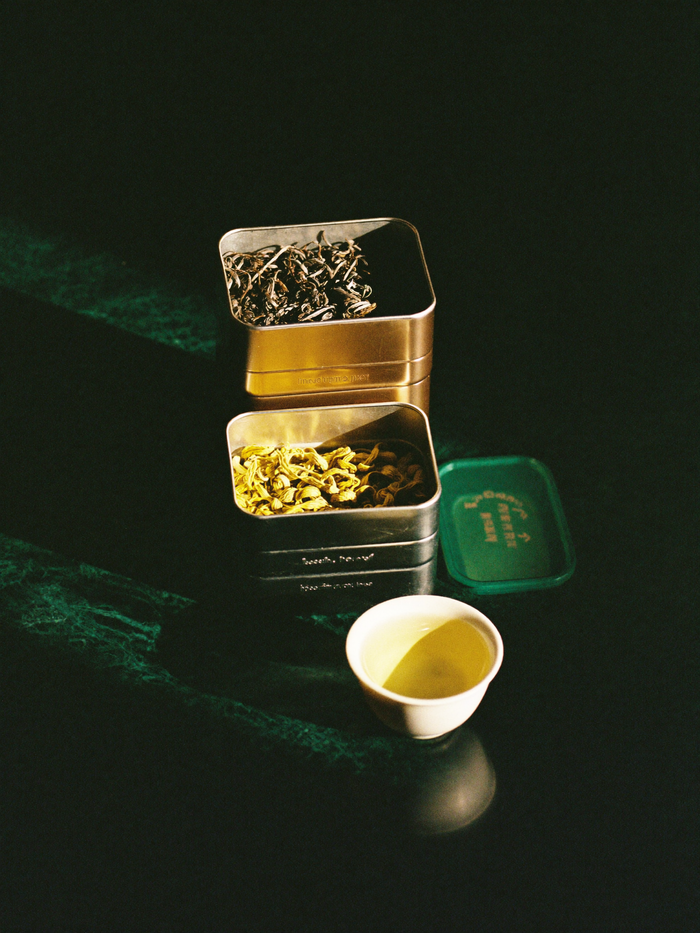 A single cup of tea steaming on polished dark marble, lit by warm golden light against a deep emerald-green background falling into shadow.