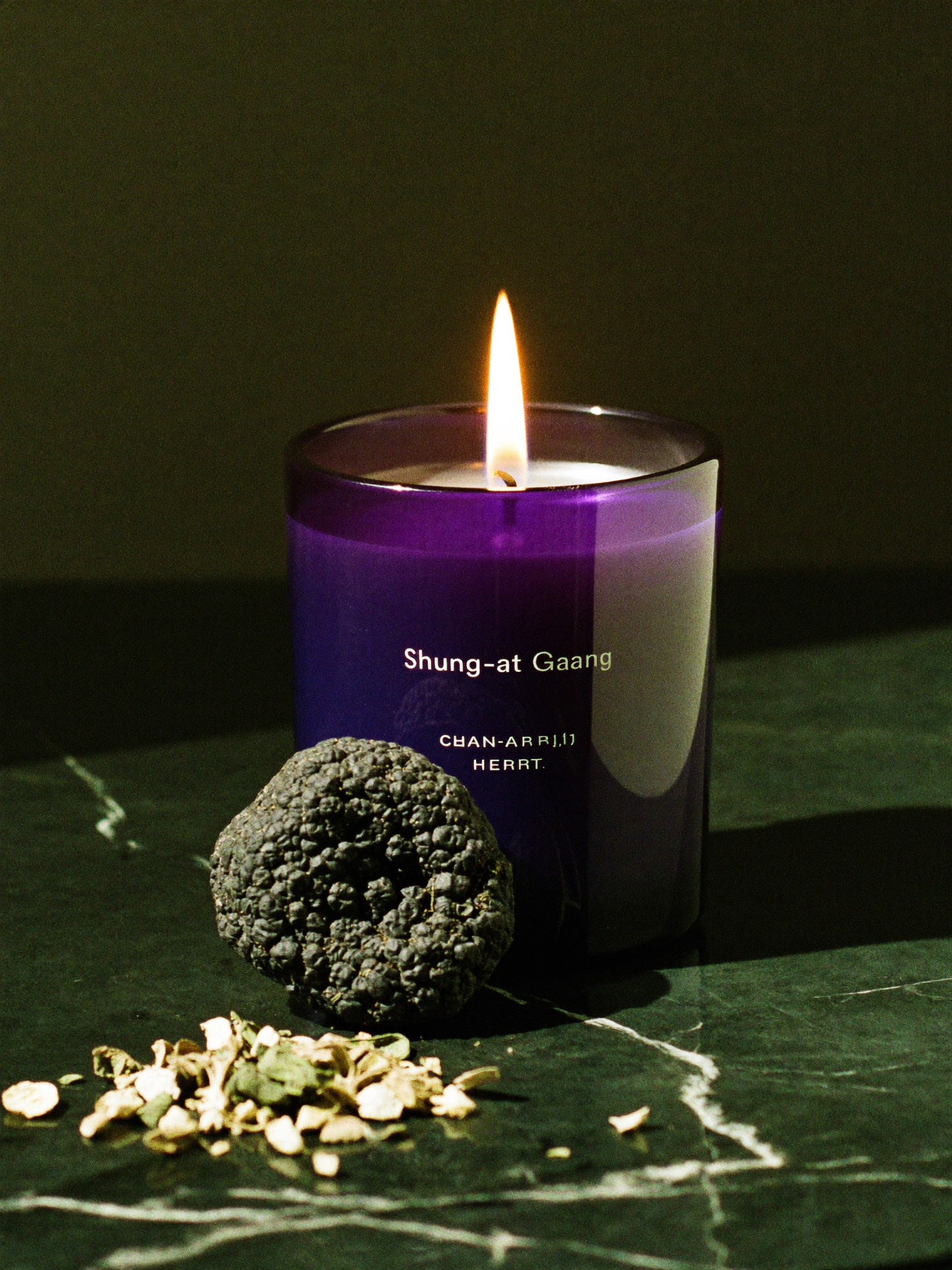 Three ritual candles arranged in a row on polished dark marble against a deep emerald-green background falling into shadow.