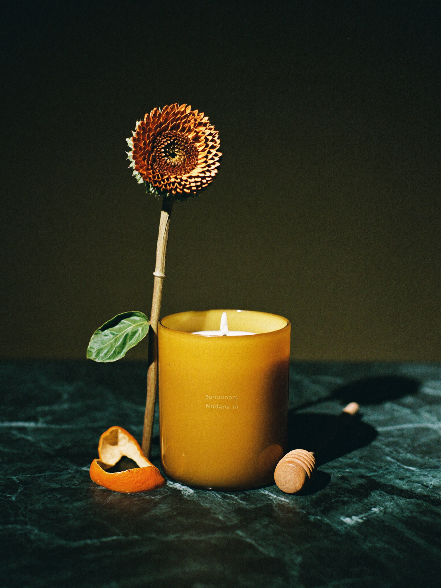Two ritual candles standing side by side on polished dark marble, lit by a single warm golden light against a deep emerald-green background.