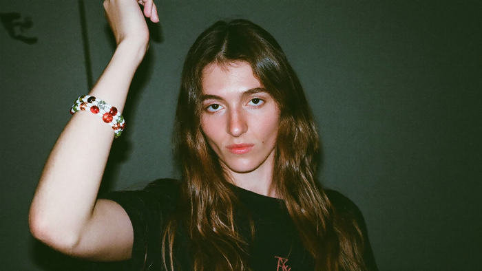 A woman wearing a beaded gemstone bracelet on her raised wrist against a dark green wall