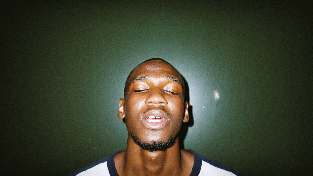 A young man with his eyes closed and head tilted back, quietly holding a sung tone
