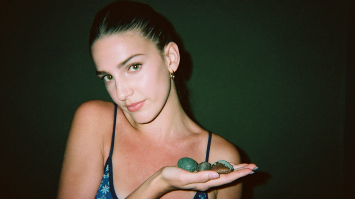 Young woman holding three smooth pebbles in an open palm against a dark green wall, direct flash portrait