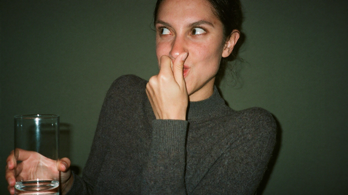 Woman pinching her nose and holding her breath with puffed cheeks to stop hiccups, a glass of water in her hand