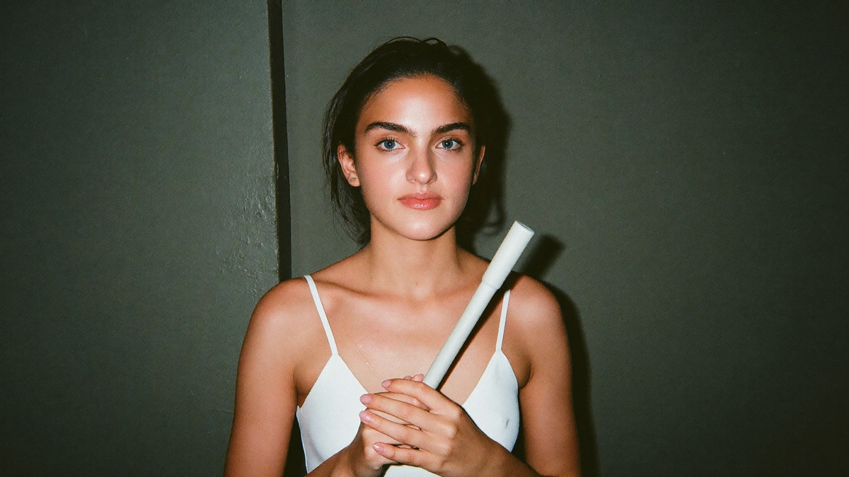 A young woman holding a white selenite wand against a dark green wall, photographed with direct flash
