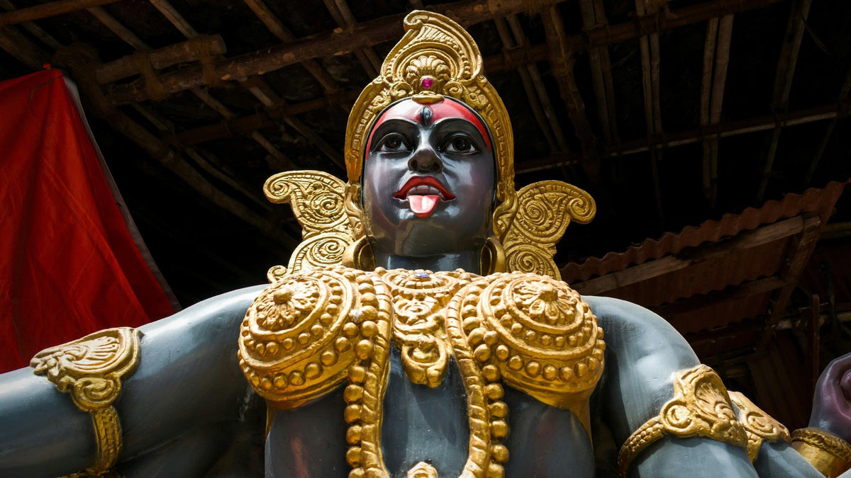 Statue of the goddess Kali with dark skin, red tongue and ornate gold crown and jewelry, seen from below