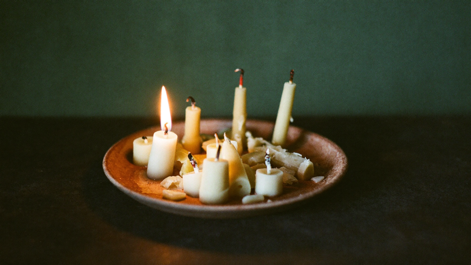 Spent candle stubs and broken pieces of leftover ritual wax gathered in a clay dish on a dark stone surface