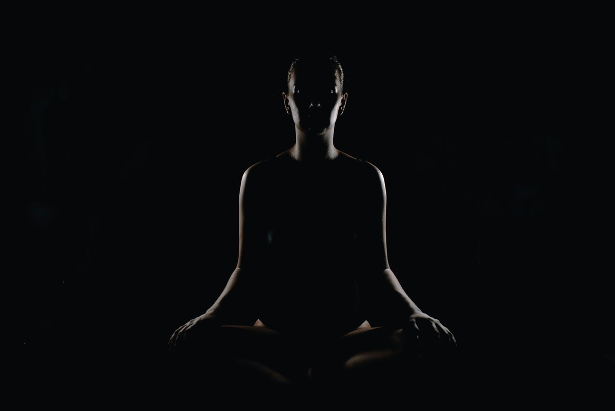 Silhouette of a person sitting cross-legged in meditation against a dark background
