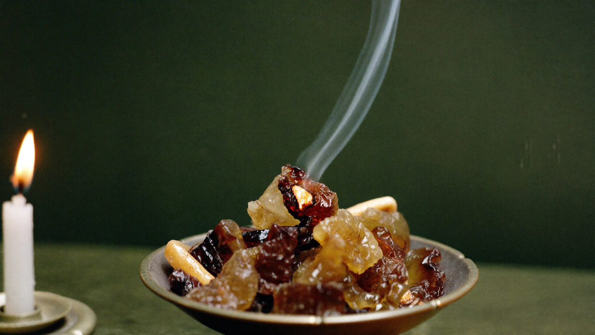 Amber and reddish brown opoponax resin tears smoking in a brass bowl beside a lit white candle