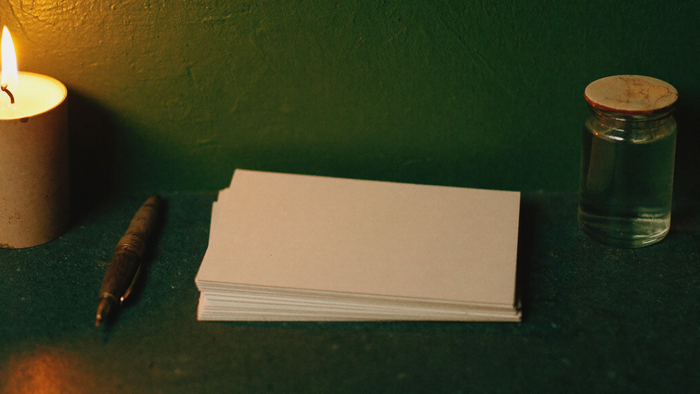 A stack of blank cards with a dip pen and glass ink bottle on a dark stone surface