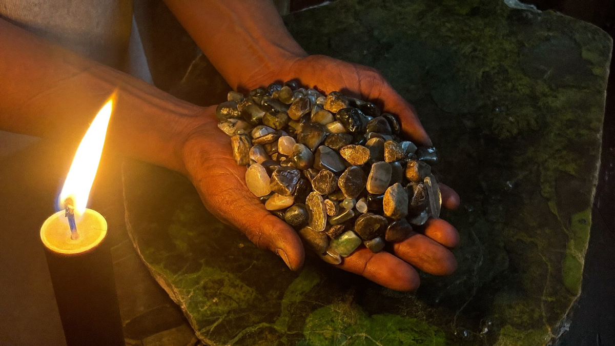 Two hands cupping a handful of collected agate and jasper pebbles by candlelight