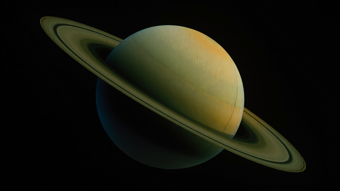 The planet Saturn with tilted rings against black space, its south pole in shadow and warm amber light along the upper edge