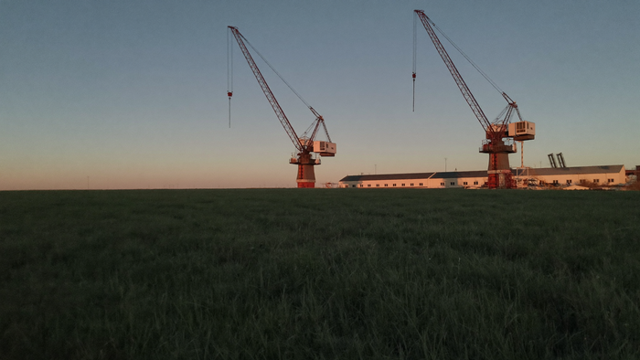 Two tall gantry cranes on rails stand above a distant test site at dusk across an open plain