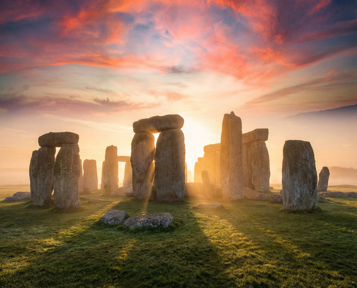 Sunrise breaking between the sarsen trilithons of Stonehenge across misty Salisbury Plain grass