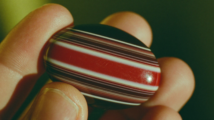 Fingers holding a polished sardonyx cabochon with straight red-brown and white bands