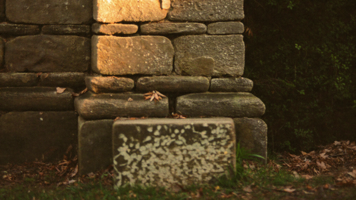 Large flat cornerstone at the foot of an old dry-stone wall, four courses of weathered masonry above it, moss in the joints