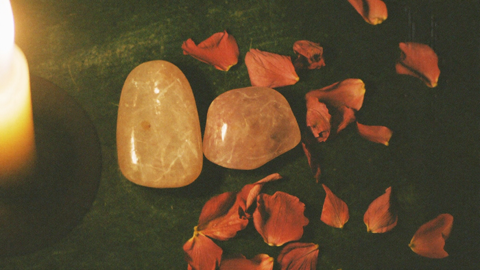 Two rose quartz stones side by side on dark stone with dried rose petals in candlelight