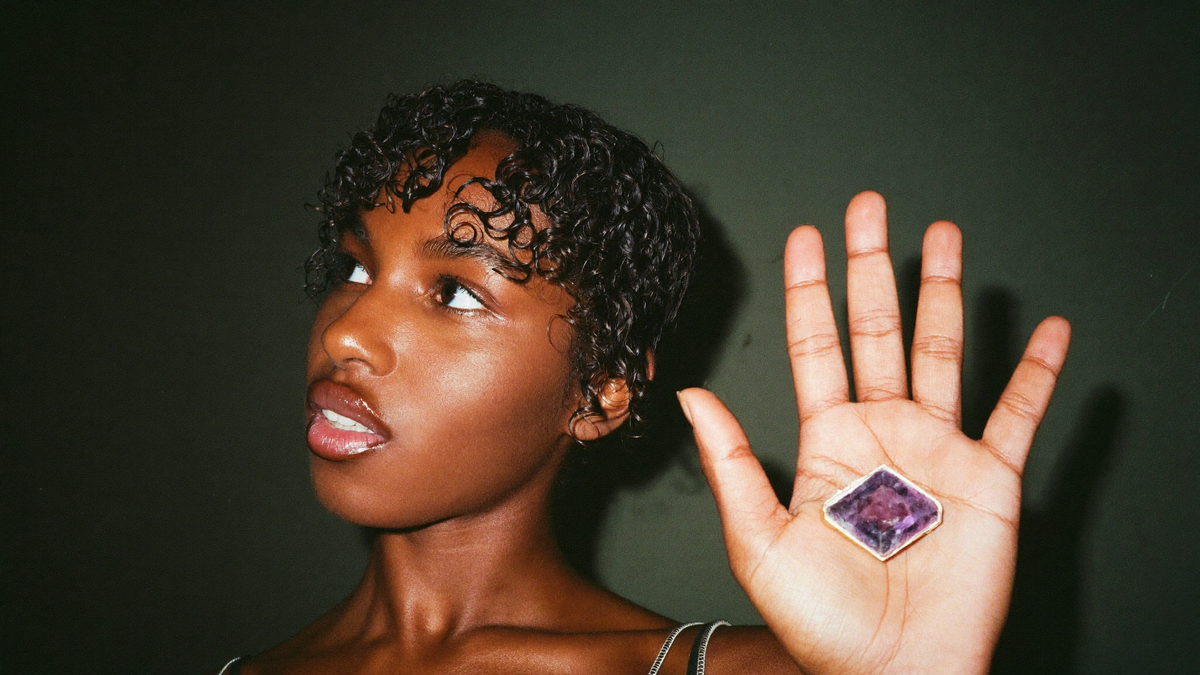 Young woman holding a polished amethyst slab in her open palm against a dark green wall