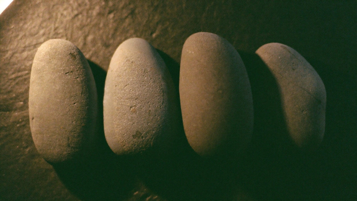 Four smooth grey river stones lined up in a row on dark slate in warm candlelight