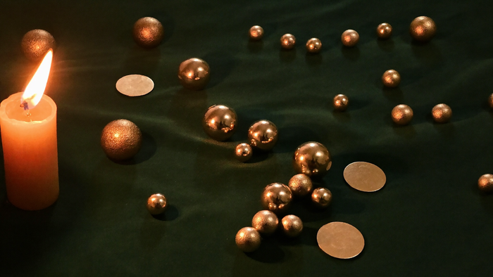 Small brass spheres scattered like planets across dark green velvet beside a single burning candle