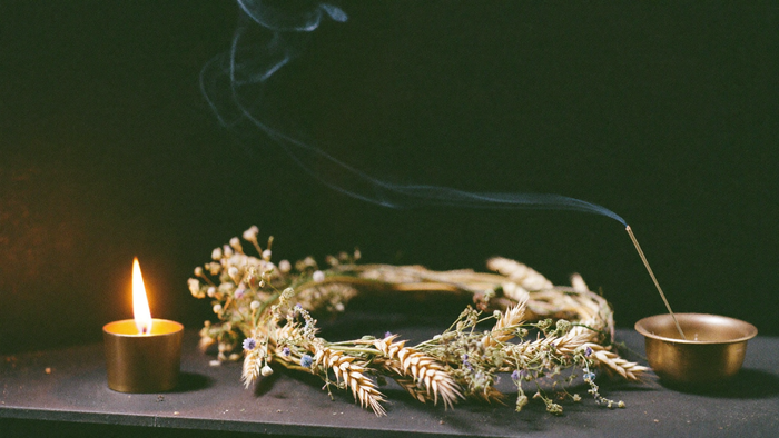 Woven wreath of dried wheat and wildflowers beside a brass tea light and a smoking incense stick