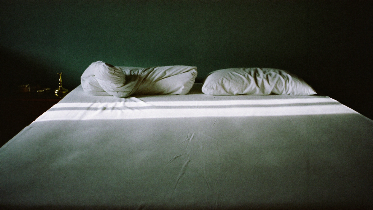An empty bed at night with the linen turned back, moonlight falling across the sheets, dark green wall behind