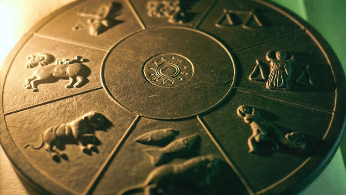 Round dark slate zodiac wheel carved with ram, bull, scales and fish reliefs, lit by warm candlelight